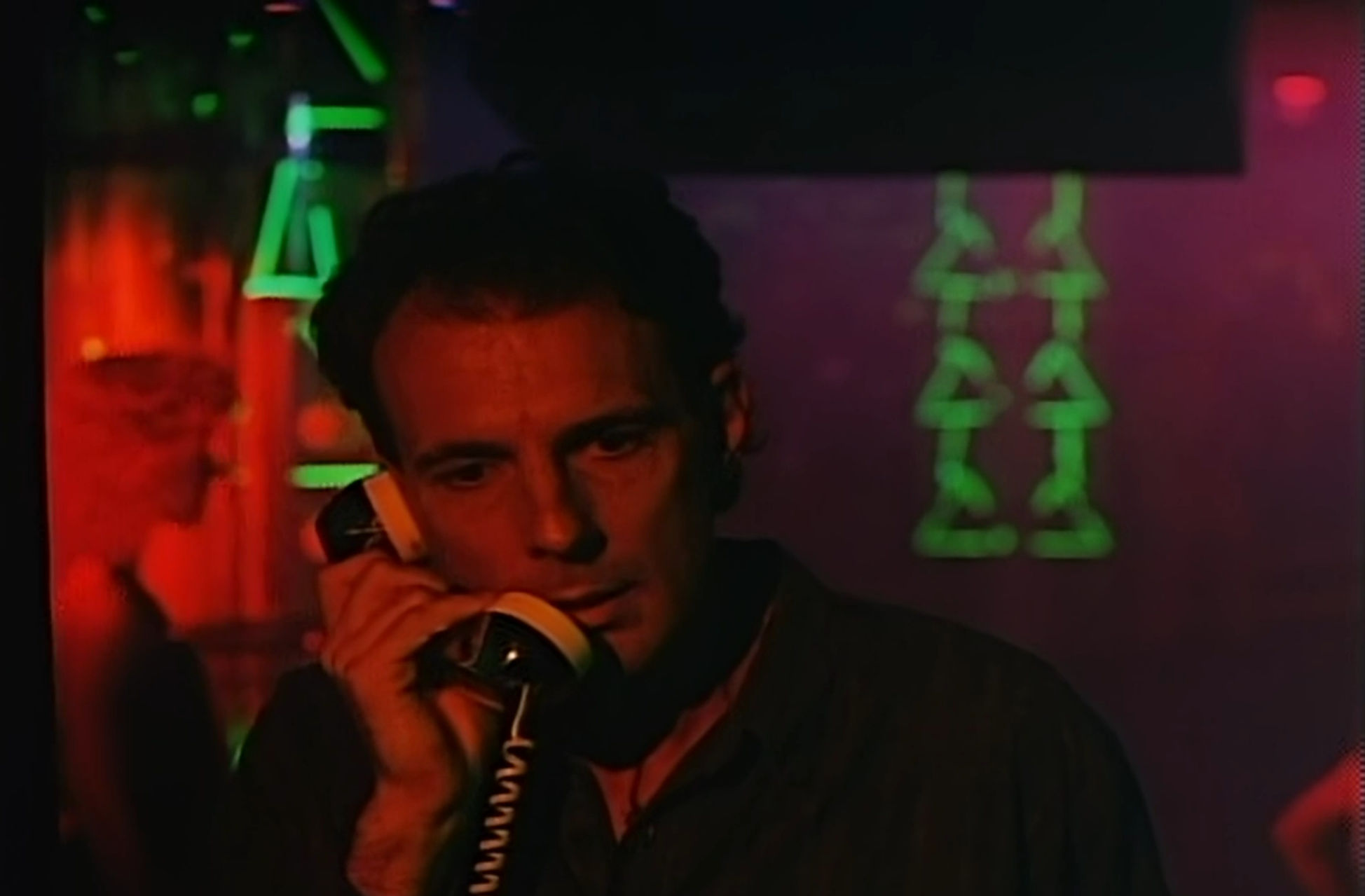 The professor making a phone call in a dimly lit, but 80s style themed, club
